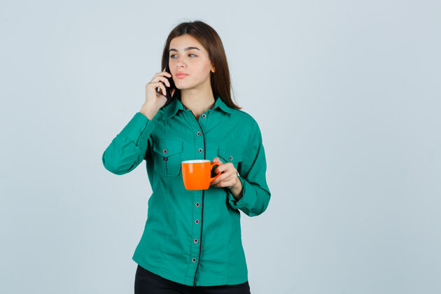 治疗一位年轻的女士端着一杯橘色的茶 穿着衬衫在讲手机 看上去很自信正面图健康女人皮肤