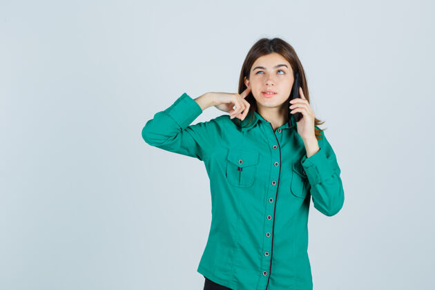 前面穿绿衬衫的年轻女士在讲手机 用手指堵住耳朵 看起来很困惑 正前方视图悲伤思考女孩