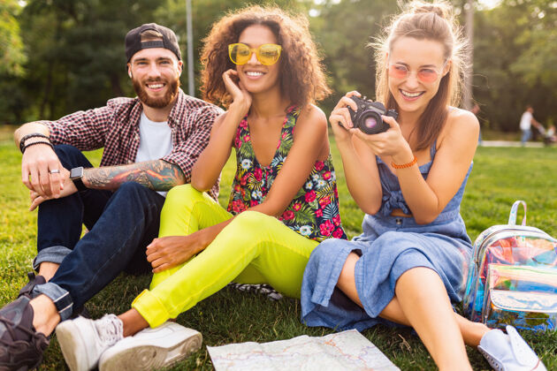 积极快乐的年轻朋友们一起坐在公园里 男女同乐 带着相机旅行 笑得坦诚女性女人欢呼