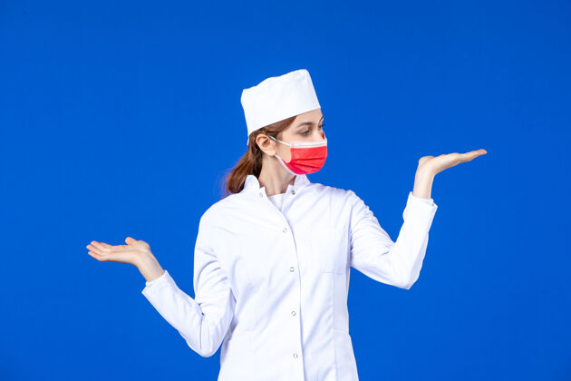 女性正面图身着医疗服的年轻护士 蓝色墙上戴着红色防护面具医学正面人