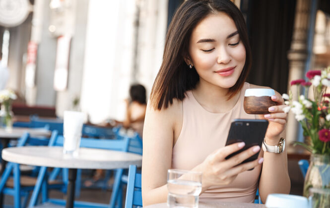 城市迷人的亚洲女人在咖啡厅休息时 微笑着用手机读着好消息休息饮用微笑
