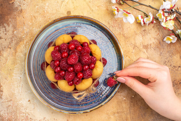 软蛋糕上图：手拿草莓放在新鲜出炉的软蛋糕上 水果放在五颜六色的桌子上食品新鲜浆果