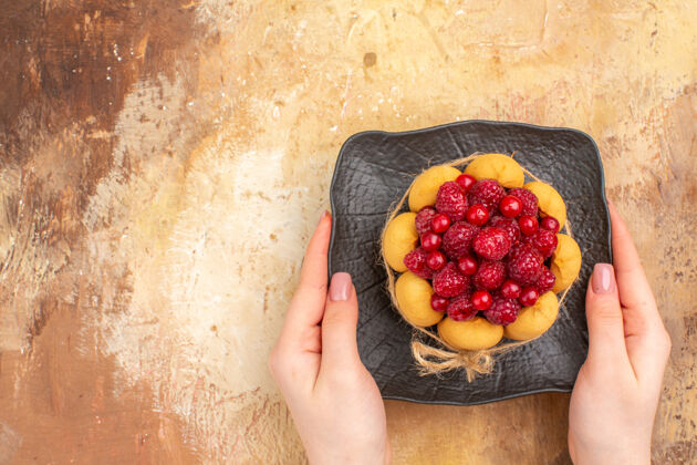 甜点手拿着刚烤好的礼品蛋糕放在一个棕色的盘子里 放在五颜六色的桌子上饮食草莓生产
