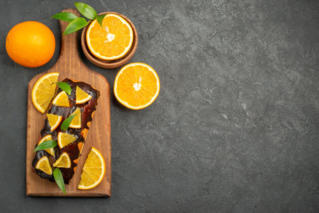 板上图：美味的蛋糕和切好的橙子放在黑桌子的砧板上切割柠檬柑橘