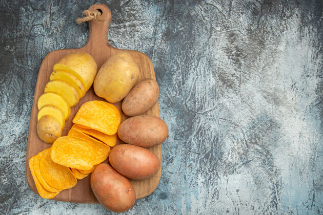 木材灰色桌子上木质砧板上的脆片和生土豆俯视图柑橘水果多汁