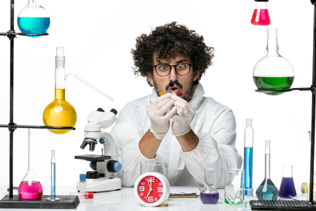 实验室正面图身着特殊套装的年轻男性科学家围着桌子工作 在白墙上摆着解决方案成人西装科学