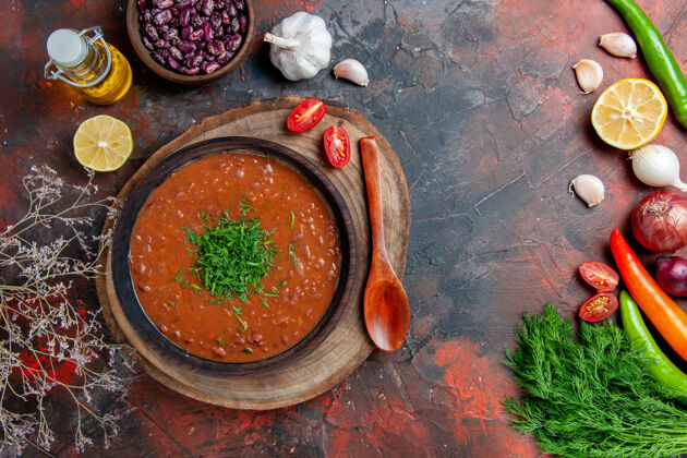 经典经典的番茄汤在一个棕色的碗里 油瓶豆子和勺子放在五颜六色的桌子上番茄混合物香料