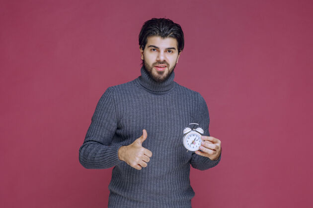 照片一个男人拿着一个白色闹钟 指着一个最好的报价模特成人职员