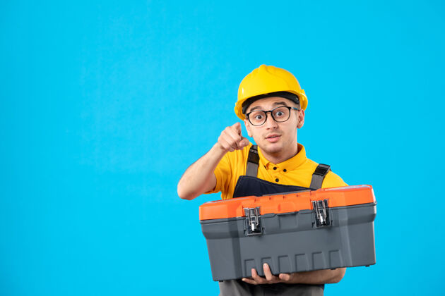 箱子身穿制服 戴着头盔 手上拿着工具箱的男工人的正视图是蓝色的工具表面服务