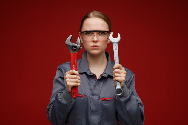 眼镜皱眉的年轻金发女工程师穿着制服 戴着护目镜拿着扳手扳手年轻女