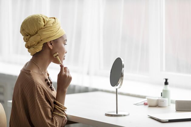女性阿拉伯妇女使用面部按摩美容治疗产品镜子平静