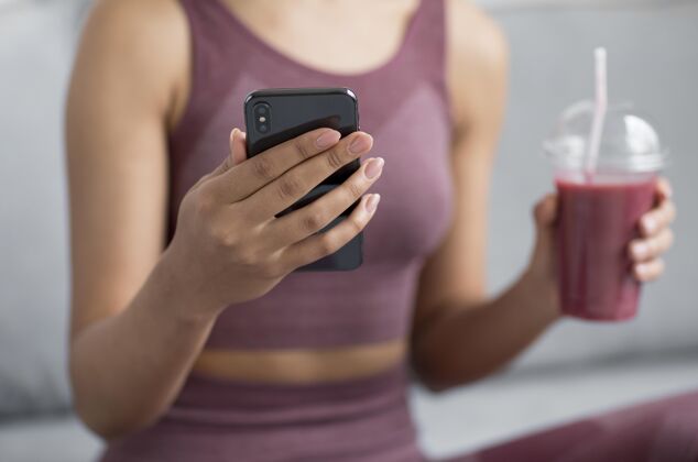 营养健身女士一边用智能手机一边喝排毒果汁房子美味果汁