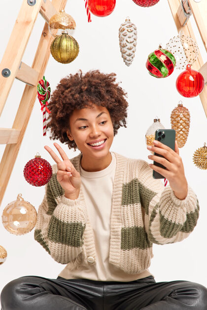 梯子快乐的非裔美国女人自拍展现和平姿态手持手机穿着休闲套头衫摆出快乐心情的姿势夏娃装饰女人