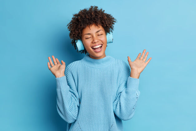 音乐积极的非洲裔美籍女性卷发扬起手掌 一边听音乐一边戴着无线耳机 穿着休闲套头衫成功耳机乐观