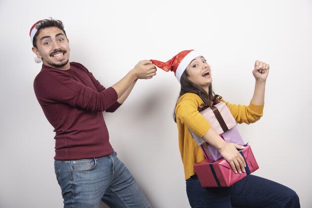 圣诞帽在白色的墙上挂着圣诞礼物的幸福夫妇人站着人类