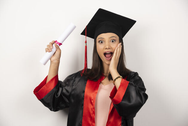 证书大学毕业的女学生在白色的背景下穿着长袍感到快乐年轻学术大学