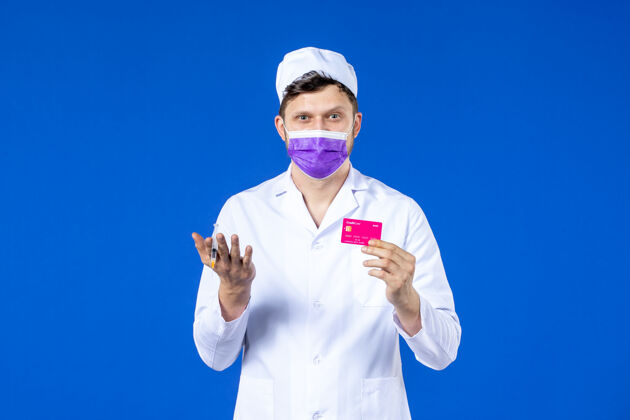 衣服前视图中的男医生穿着医疗服和紫色面罩持有注射和信用卡在蓝色实验室外套注射药