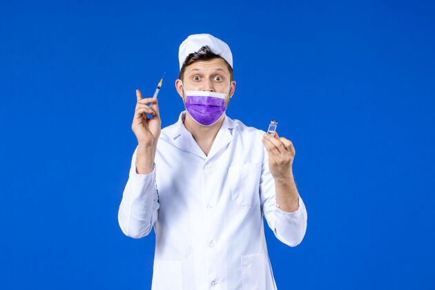 注射前视图中的男医生穿着医疗服和口罩持有疫苗和注射在蓝色药品疫苗医院
