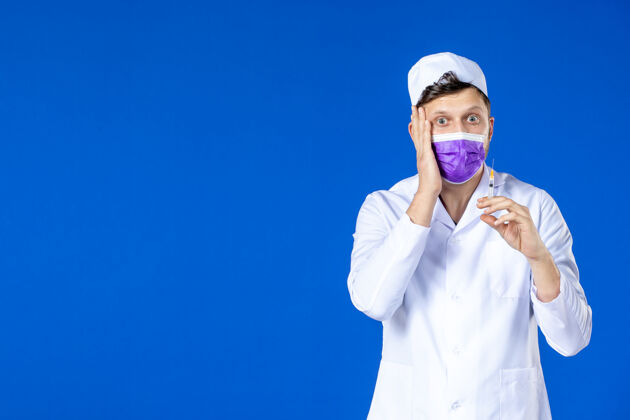 套装前视图中的男医生穿着医疗服和面具举行注射蓝色医院注射药品