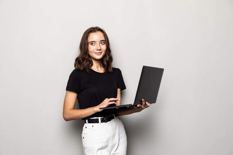 博客一个快乐的惊讶的女人站在灰色的墙上 笔记本电脑被隔离笔记本漂亮青少年