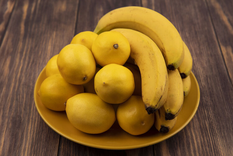 片黄色盘子上新鲜的黄皮柠檬的顶视图 木头表面放着香蕉新鲜木头柠檬