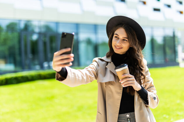 自我年轻漂亮的女学生穿着外套戴着帽子拿着咖啡去街上打电话自拍电话约克乐趣