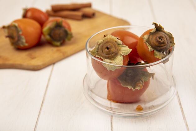 食物白色木质表面上的玻璃碗上新鲜多汁的柿子的俯视图午餐饮食健康