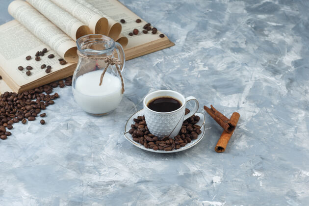 热用咖啡豆 书 肉桂棒 牛奶在一个灰色灰泥背景上高角度观看一杯咖啡味道杯子人