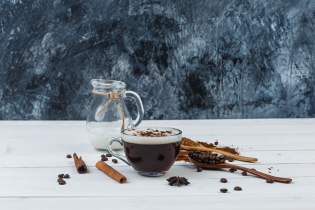 早晨咖啡在一个杯子与研磨咖啡 咖啡豆 肉桂棒 牛奶侧视图在木制和垃圾的背景种子自然垃圾