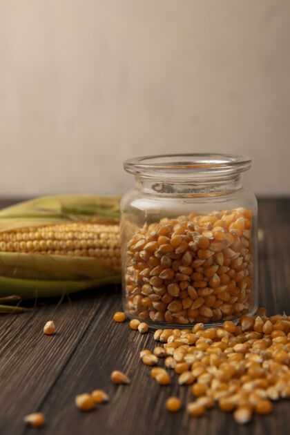 新鲜侧视图的有机和新鲜玉米粒上的玻璃罐与谷粒隔离在一个木墙上木材配料玉米