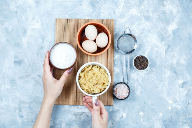 食物手拿着一碗碗酸奶和意大利面 上面放着鸡蛋 粗滤器 调味品 平躺在肮脏的灰色和砧板背景上蔬菜新鲜咕噜