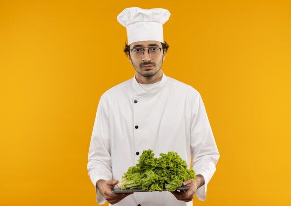 板年轻的男厨师穿着厨师制服 戴着眼镜 在砧板上拿着沙拉男性制服削减