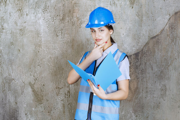 思维女工程师身穿蓝色制服 头戴安全帽 手里拿着蓝色报告夹 看上去很体贴晋升模型分析