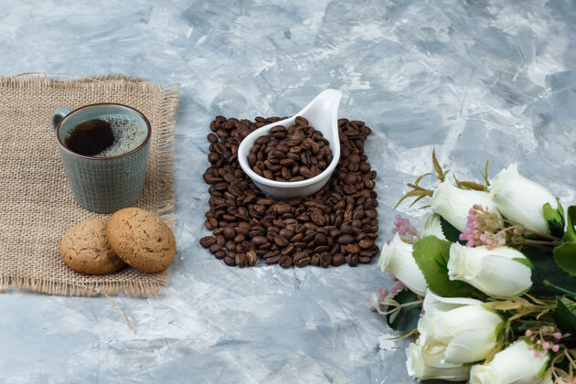 卡布奇诺一套饼干 一杯咖啡 鲜花和咖啡豆放在一个蓝色大理石背景的白色瓷罐里特写镜头瓷器花咖啡