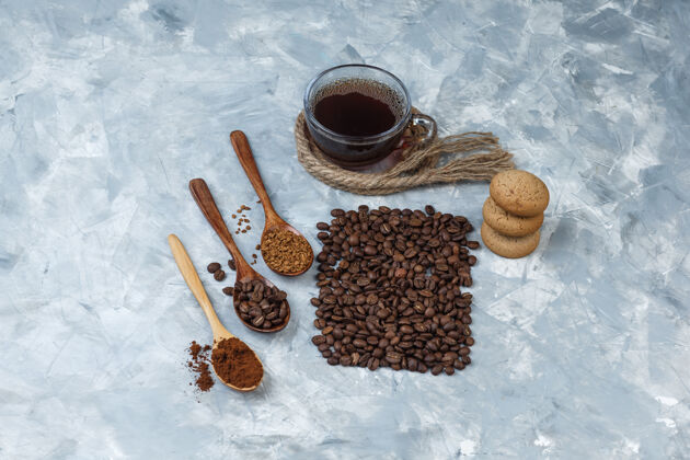 速溶一套咖啡豆 速溶咖啡 咖啡粉在木制勺子 绳子 饼干和咖啡豆 咖啡杯浅蓝色大理石背景平放绳子意式咖啡木头