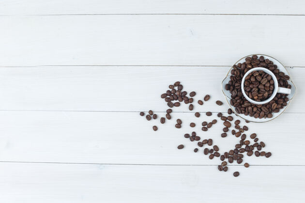 配料咖啡豆在茶杯和茶碟顶视图在木制背景上种子木材