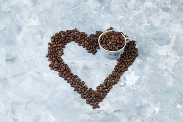 堆咖啡豆在一个灰色灰泥背景杯高角度的看法阿拉比卡香味