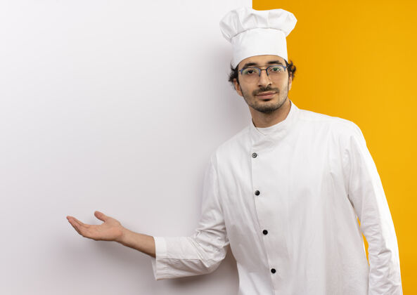 演示年轻的男厨师穿着厨师制服 戴着眼镜 手拿白墙年轻白色墙壁