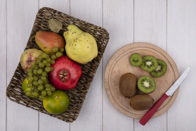 苹果顶视图猕猴桃用刀放在砧板上 橘子石榴梨苹果和葡萄放在白色墙上的篮子里板新鲜梨
