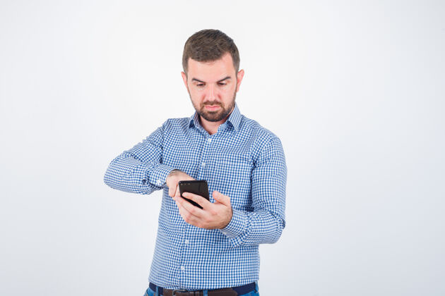 自由职业者概念照片中的年轻男性穿着衬衫 牛仔裤看着手机 目光集中在前视图上电话男人锻炼