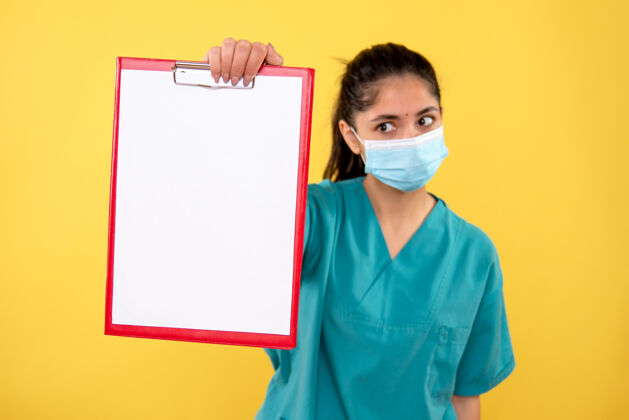 年轻前视图穿着制服的年轻女医生展示了站在黄色背景上的剪贴板前面剪贴板医学