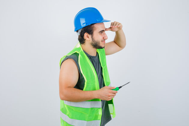 人员年轻的建筑工人手里拿着螺丝刀 手放在头上 看得很清楚 穿着制服 看起来很高兴前视图工作头部保持