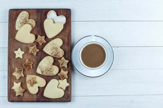 美味平放心形和星形饼干在木制砧板上 咖啡杯在白色木板背景上水平咖啡生日木头