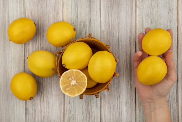 美味顶视图的女性手拿着柠檬与柠檬在一个灰色的木制表面桶持有健康柑橘