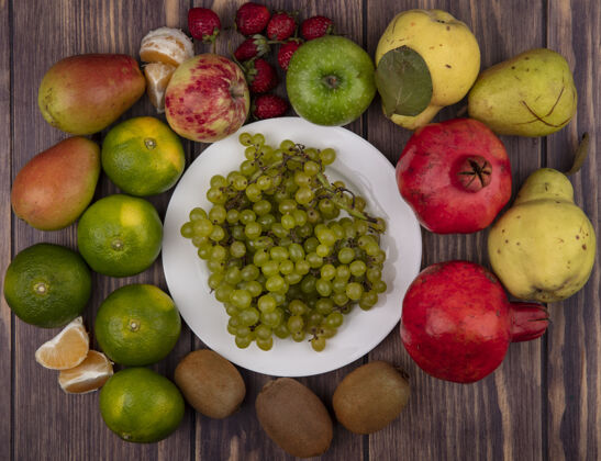 食物顶视图绿色葡萄放在一个盘子里 猕猴桃 橘子 梨 草莓和石榴放在木墙上顶梨橘子