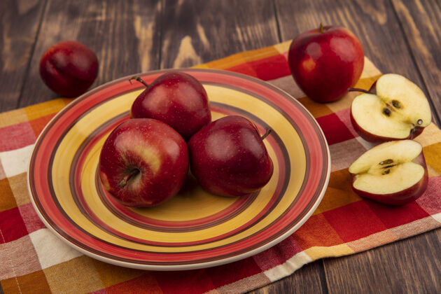 美味多汁的红苹果在格子布盘子上的俯视图 一半的苹果被隔离在木头表面农业多汁配料