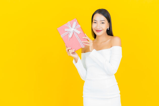 礼物黄墙上挂着红色礼盒的亚洲商界年轻美女画像人漂亮脸