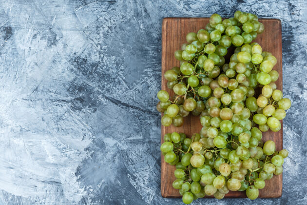成熟绿色的葡萄在粗糙的灰泥和砧板背景上平放素食多汁食物