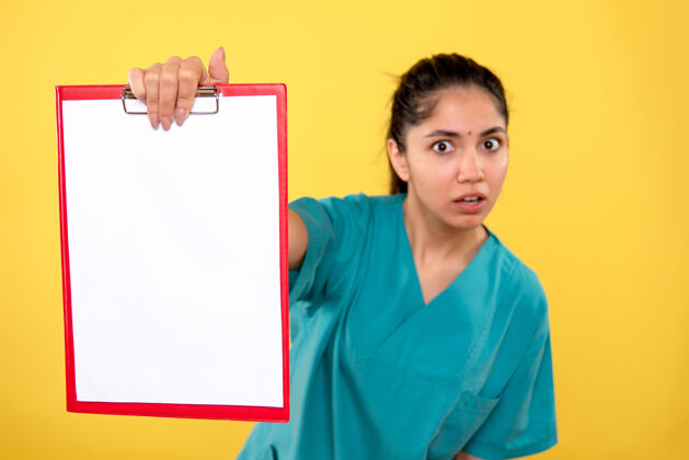 背景前视图漂亮的女医生穿着制服 剪贴板站在黄色背景上站工作专业
