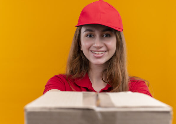 制服微笑着的年轻送货女孩穿着红色制服 在孤立的橙色墙上伸出盒子微笑分娩伸展